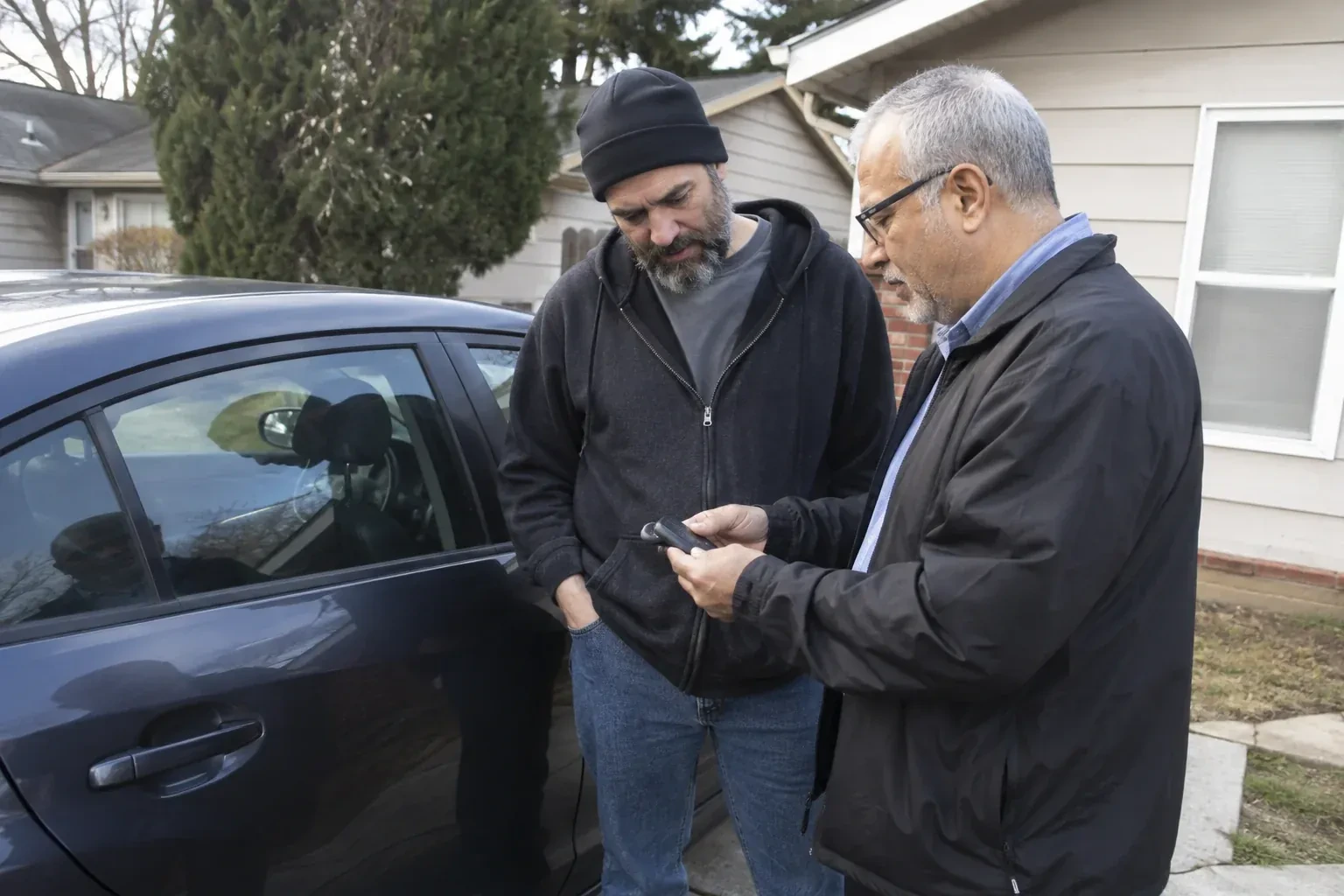 Two adults discussing a key fob beside a parked car. — Car Lockout Service, New Tecumseth
