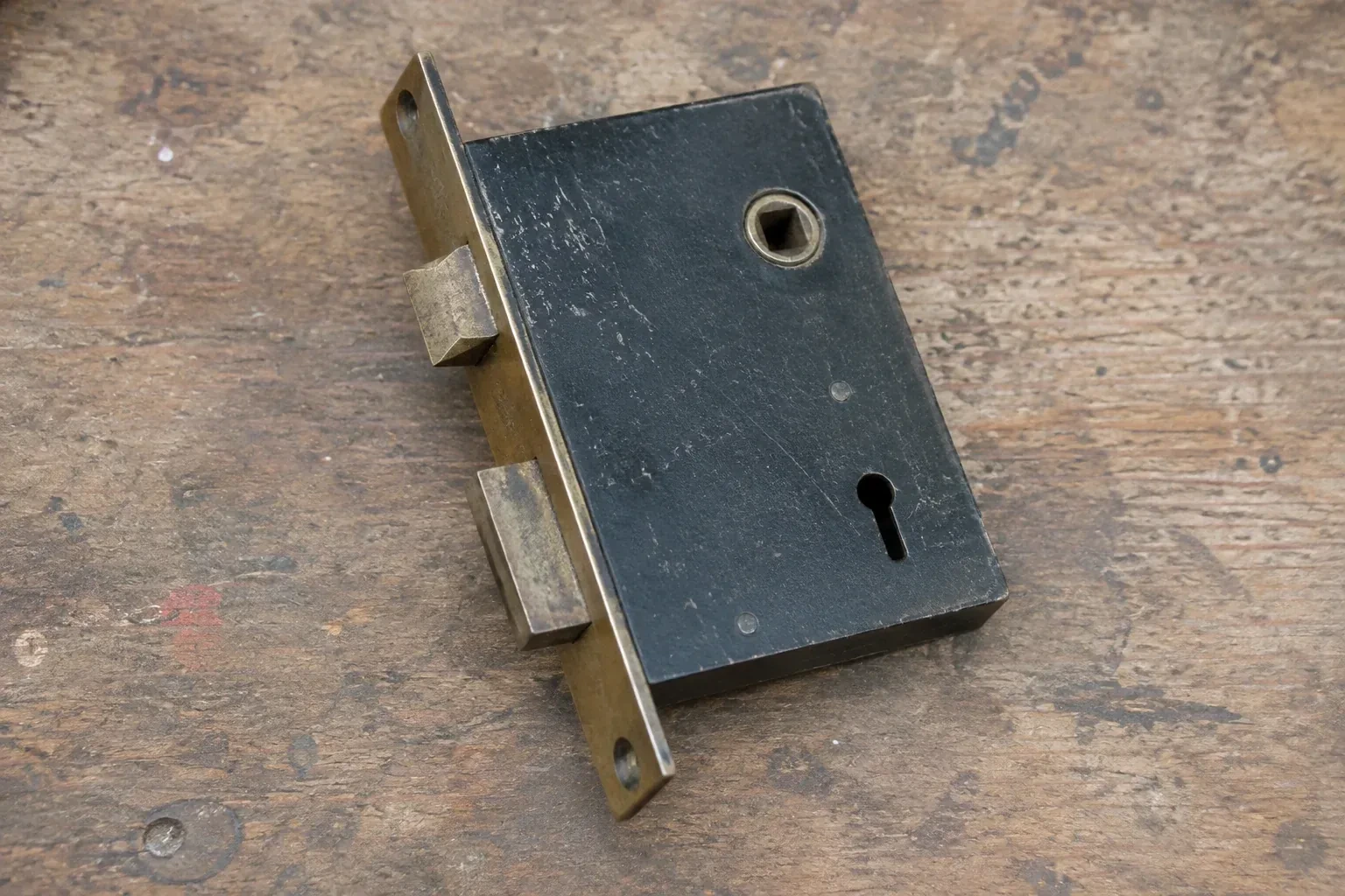 Closed mortise lock case with spindle opening, keyhole, latch and deadbolt on a wooden workbench. — Vintage Mortise Lock Service, New Tecumseth